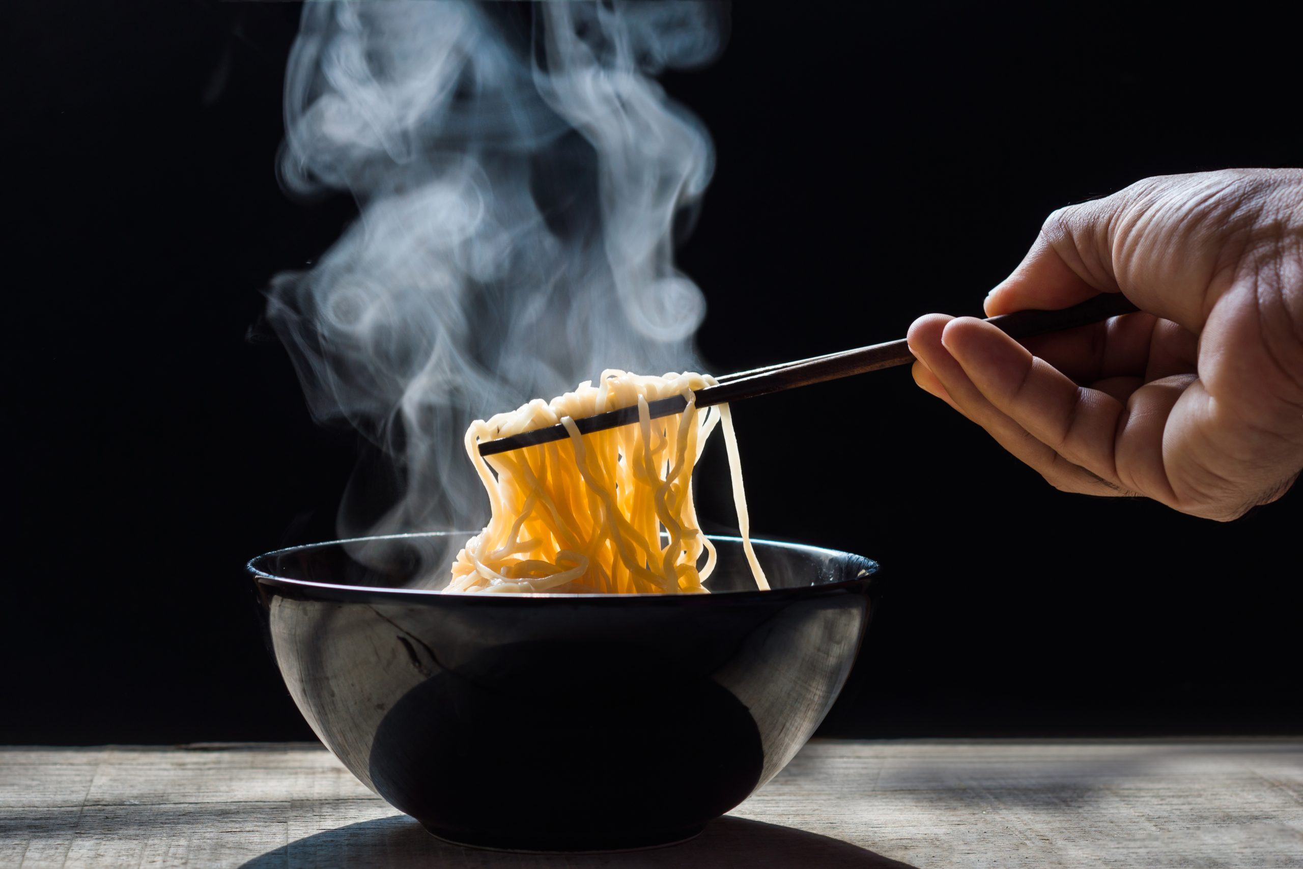 Hand uses chopsticks to pickup tasty noodles with steam and smok